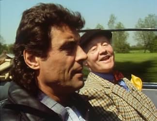 Lovejoy driving with Tinker beside him in tweed, hat and yellow buttonhole, on a sunlit country road